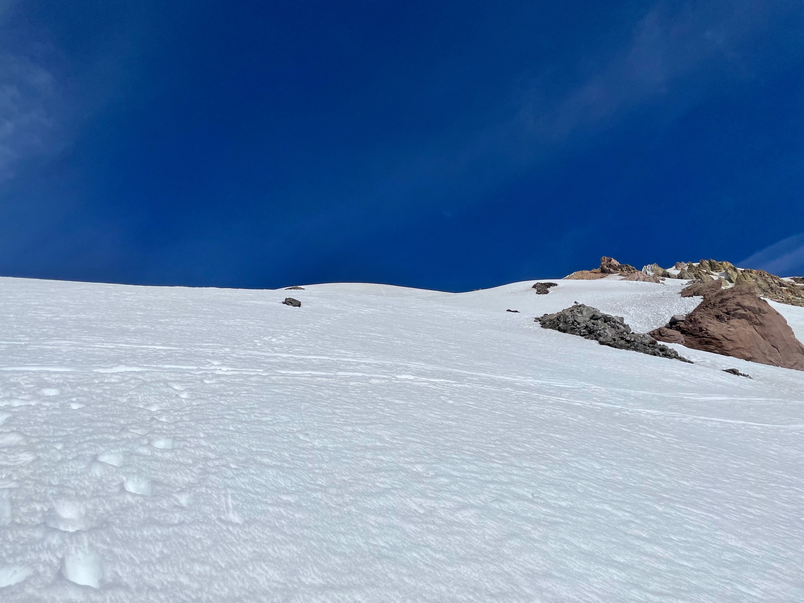 Small foot holds punched into a steep snow face, receding uphill towards the summit.